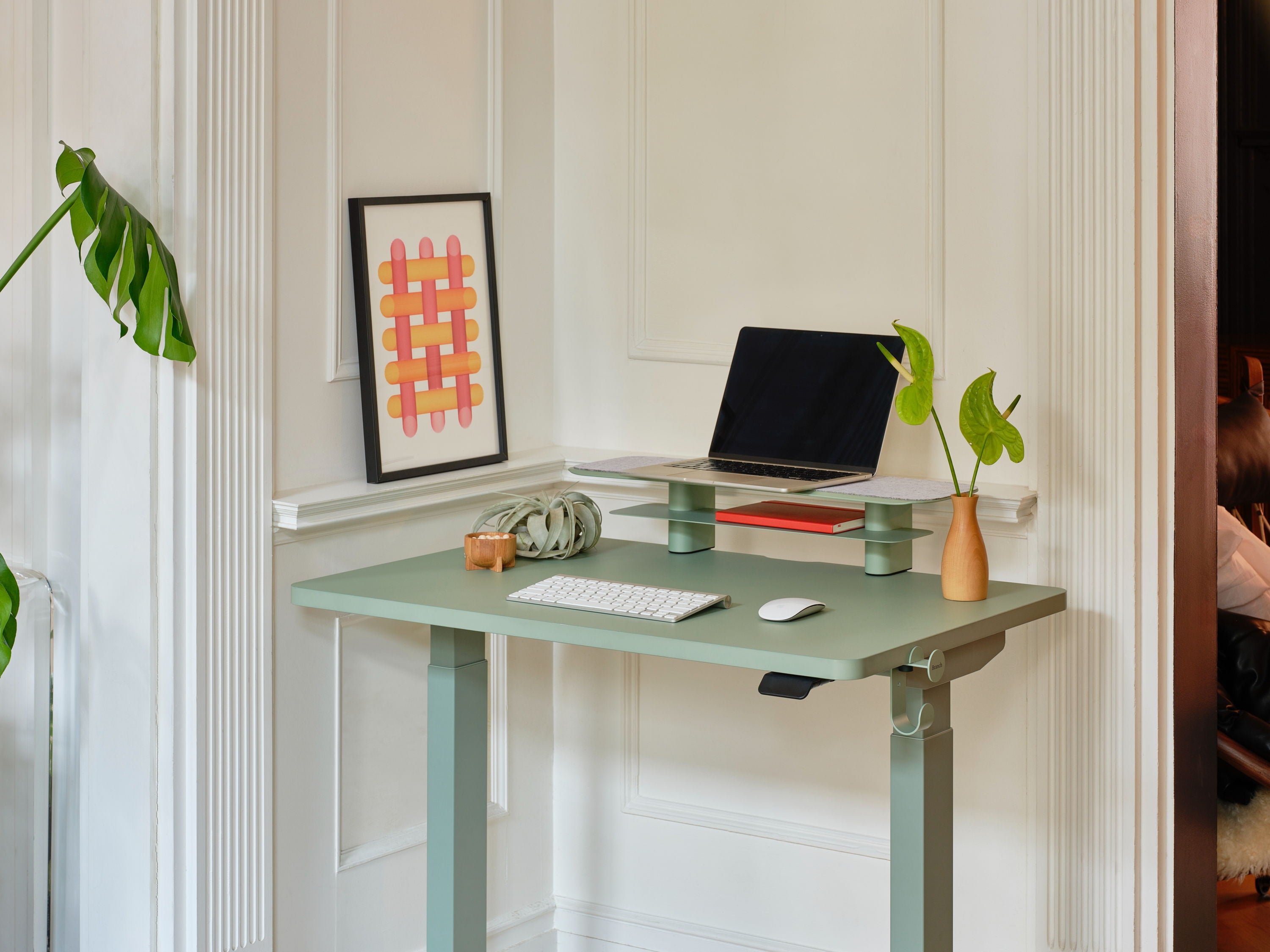A modern desk with a laptop, plants, and artwork on the wall.