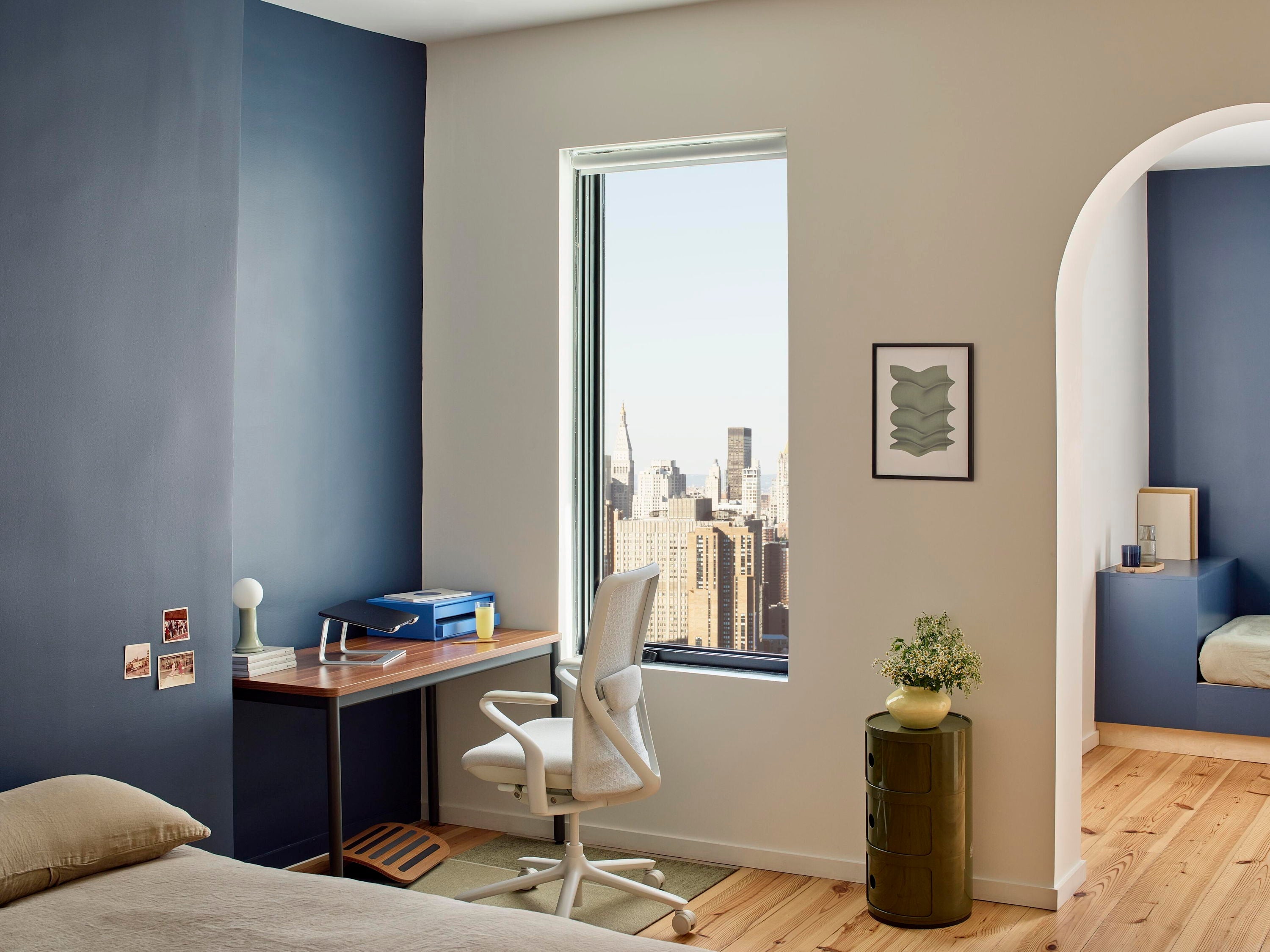 Modern bedroom with a desk, chair, and a city view window.
